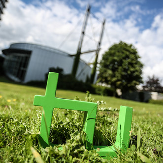 Im Vordergrund steht das TU-Logo im Gras, im Hintergrund das Audimax.