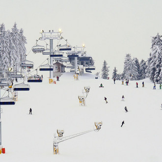 Verschneite Skipiste in Winterberg, mit Sessellift, Schneekanonen und vielen Skifahrern.