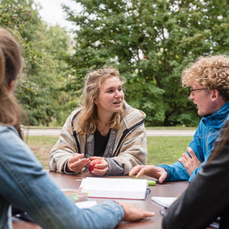 Vier Studierende sitzen draußen an einem Tisch und lernen zusammen.
