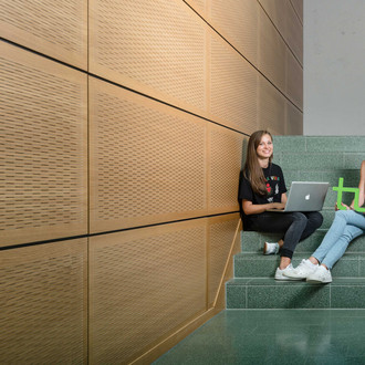 Zwei Studentinnen sitzen mit Laptop und TU-Logo auf einer Treppe.