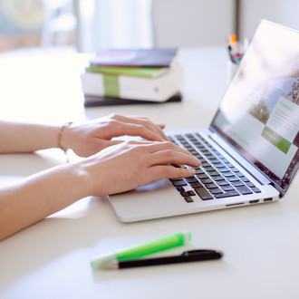 Studentin tippend am Laptop, daneben liegen Bücher und Stifte.