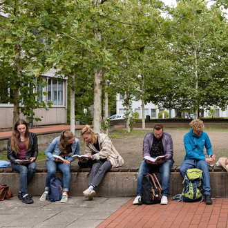 Sechs Studierende sitzen auf einer langen Bank auf dem Campus Süd.