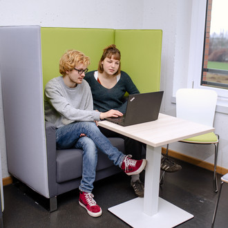 Zwei Studierende sitzen auf einem Sessel und sehen auf einen Laptop vor ihnen.