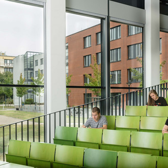 Drei Studierende sitzen in einem grün bestuhlten Hörsaal.