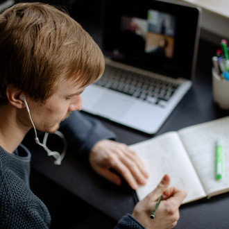 Ein Student arbeitet mit Laptop und Notizbuch.