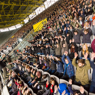 Studierende des ersten Semesters sitzen im Stadium auf den Rängen während der Erstsemesterbegrüßung und starten eine Laolawelle.