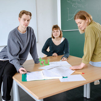 Drei Studierende im Seminarraum sitzen um einen Tisch herum und arbeiten