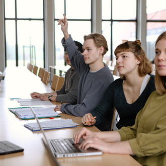 Studierende in einem Seminarraum, ein Student meldet sich