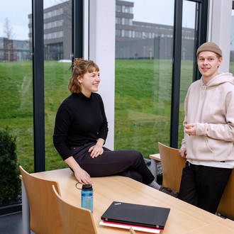 Zwei Studierende im Seminarraum unterhalten sich miteinander