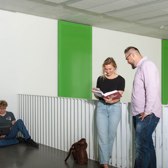 Zwei Studierende stehen vor einem Geländer und sehen in ein Buch.