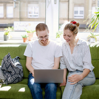 Zwei Studierende arbeiten am Laptop, auf einem Sofa sitzend.
