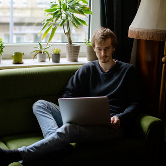 Ein Student, auf dem Sofa sitzend, arbeitet am Laptop.