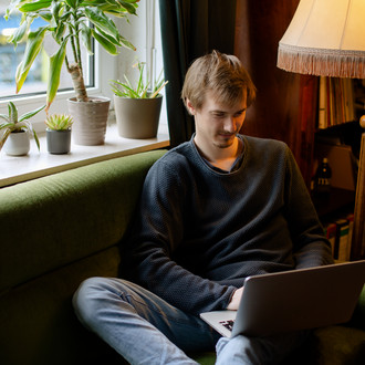 Ein Student, auf dem Sofa sitzend, arbeitet am Laptop.