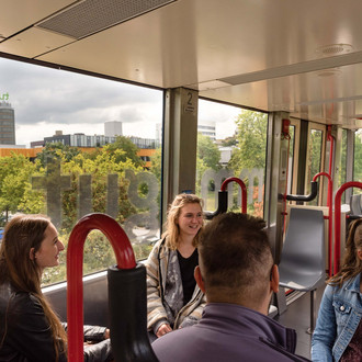 Vier Studierende sitzen sich gegenüber in der H-Bahn und unterhalten sich.