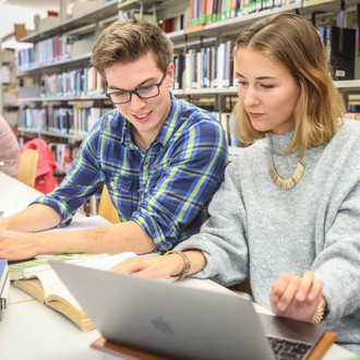 Drei Studierende sitzen an einem Tisch in der Bibliothek und arbeiten.