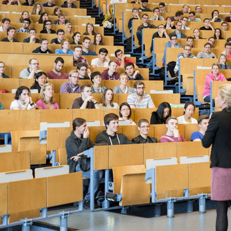 Eine Dozierende steht vor Studierenden in der Vorlesung im Hörsaal. 