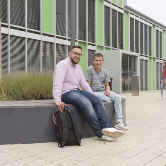 Studierende sitzen vor einem Gebäude.