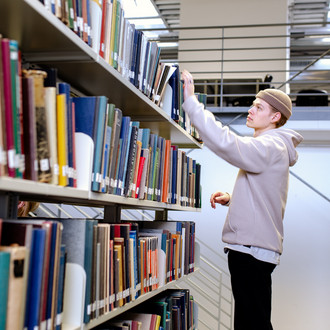 Ein Studierender steht suchend an einem Bücherregal in der Bibliothek.