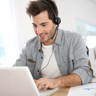 Mann sitzt vor dem Laptop und hat ein Headset auf.