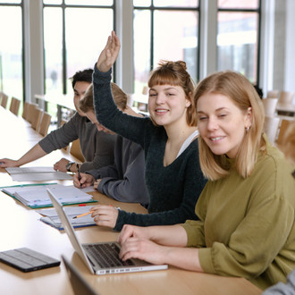 Studierende im Seminarraum sitzen in einer Tischreihe vor ihren Laptops. 