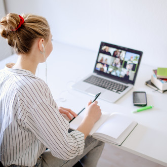 Am Schreibtisch sitzende Studentin schaut Lernvideos, daneben liegen Bücher und Stifte.