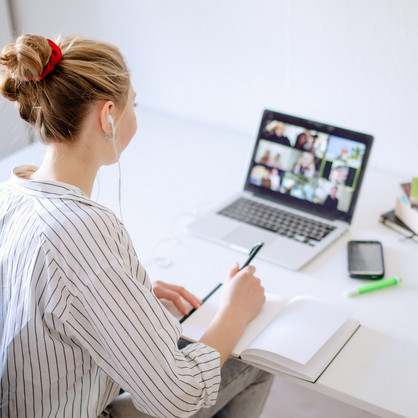 Am Schreibtisch sitzende Studentin schaut Lernvideos, daneben liegen Bücher und Stifte.