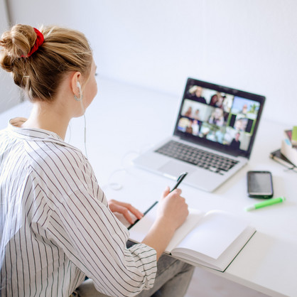 Student sitting at desk watching learning videos, books and pens next to her.