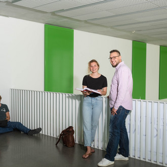 Zwei Studierende stehen vor einem Geländer und sehen in die Kamera.
