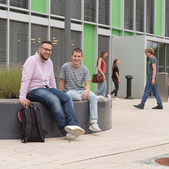 Studierende sitzen vor einem Gebäude.