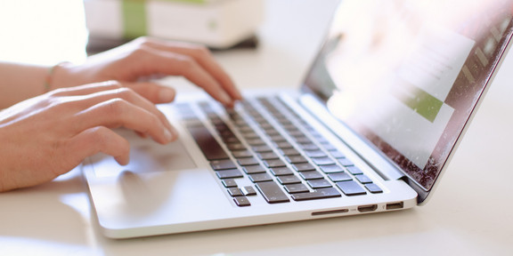 Studentin tippend am Laptop, daneben liegen Bücher.