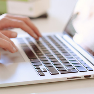 Studentin tippend am Laptop, daneben liegen Bücher.