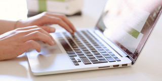 Studentin tippend am Laptop, daneben liegen Bücher.