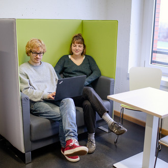 Zwei Studierende sitzen in einem Sessel. 