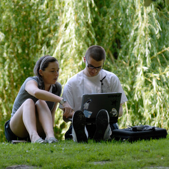 Eine Studentin und ein Student beim gemeinsamen Lernen mit Laptop auf einer Wiese im Sommer