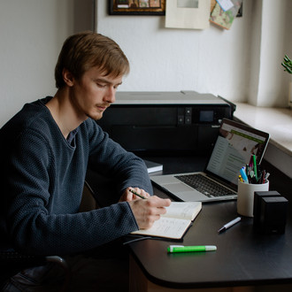 Ein Student arbeitet mit Laptop und Notizbuch.