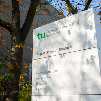 Infotafel der TU Dortmund an der August-Schmidt-Straße umgeben von Bäumen.
