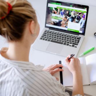 Am Schreibtisch sitzende Studentin arbeitet am Laptop, daneben liegen Bücher und Stifte.