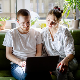 Zwei Studierende arbeiten am Laptop, auf einem Sofa sitzend.