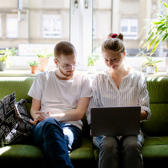 Zwei Studierende arbeiten am Laptop, auf einem Sofa sitzend.