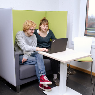 Zwei Studierende sitzen auf einem Sessel und sehen auf einen Laptop vor ihnen.