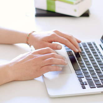 Studentin tippend am Laptop, daneben liegen Bücher.