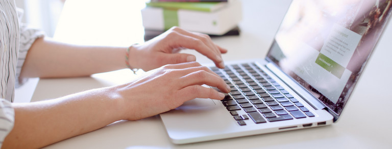 Studentin tippend am Laptop, daneben liegen Bücher.