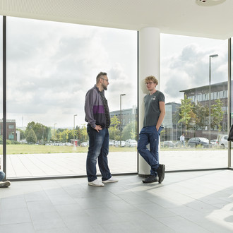 Studierende im Gespräch vor einem großen Fenster.