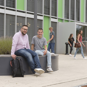 Studierende sitzen vor einem Gebäude.