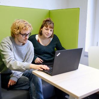 Zwei Studierende sitzen auf einem Sessel und sehen beide auf einen Laptop vor ihnen.