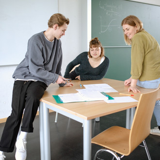 Drei Studierende im Seminarraum sitzen um einen Tisch und arbeiten gemeinsam
