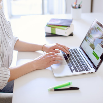 Studentin tippend am Laptop, daneben liegen Bücher und Stifte.