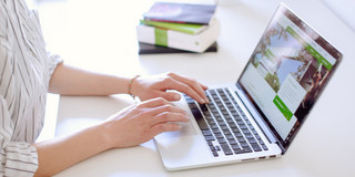 Studentin tippend am Laptop, daneben liegen Bücher und Stifte.