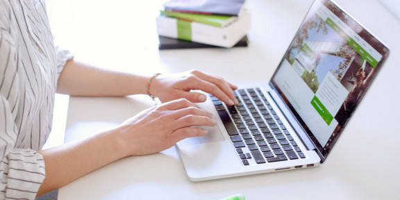 Arbeit am Laptop Studentin tippend am Laptop, daneben liegen Bücher und Stifte.