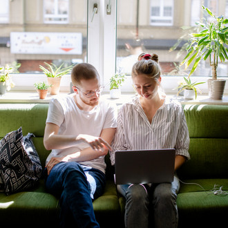 Zwei Studierende arbeiten am Laptop, auf einem Sofa sitzend.